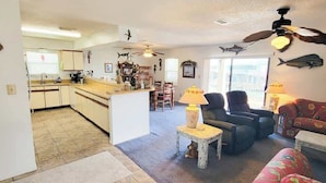 A spacious living area with a sofa, chairs, and a dining table. There is a kitchen in the background with cabinets and a countertop.