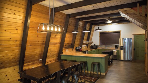 Une cuisine chaleureuse avec des murs en bois, un îlot central, des tabourets de bar et des luminaires suspendus.