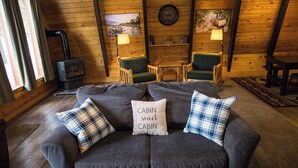 L’intérieur d’un chalet accueillant, avec un canapé, deux fauteuils, un mur en bois, une cheminée et une horloge.