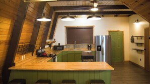 Une cuisine avec un îlot central en bois, des armoires vertes et un réfrigérateur en acier inoxydable.