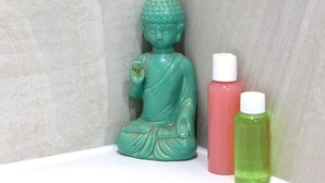 Ein Badezimmer mit einer grünen Buddha-Statue, einer rosa und einer grünen Flasche.