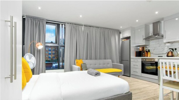 Ein modernes Schlafzimmer mit einem großen Bett, einem grauen Sofa und einem Essbereich mit einem weißen Tisch und Stühlen.