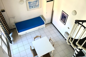 Une petite pièce comprenant un lit, une table, des chaises, un escalier et un tableau accroché au mur.