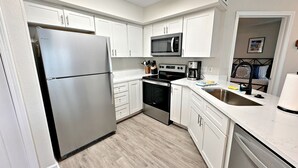 A modern kitchen with white cabinets, stainless steel appliances, and a wooden floor.