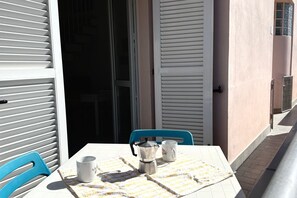 A table with a coffee pot and two cups, a blue chair, and a white tablecloth.
