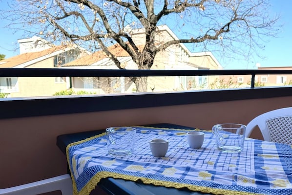 A balcony with a table set for two, a view of houses, and a tree.