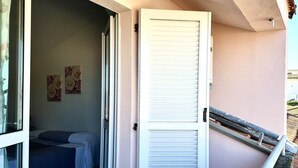 Una stanza con un letto, una porta bianca e un balcone con ringhiera.