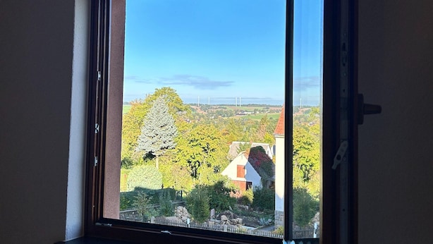 A view through a window with a clear sky, a tree, and a building with a red roof. - Schlossblick und Komfort in Stolpen (Stolpen)