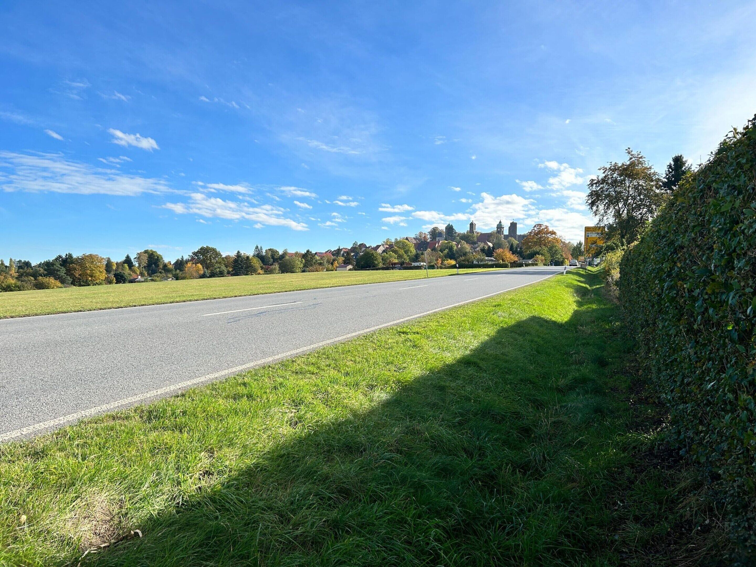 A straight road with a grassy median, trees, and a clear blue sky.