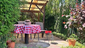 An outdoor patio with a checkered tablecloth, a wooden pergola, and potted plants. - Schlossblick und Komfort in Stolpen (Stolpen)