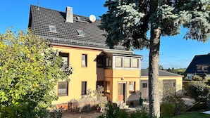 A two-story house with a sloped roof, a satellite dish, and a large tree in the foreground. - Schlossblick und Komfort in Stolpen (Stolpen)