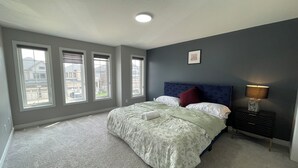 A bedroom with a bed, a nightstand, a lamp, and three windows.