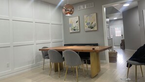 A dining area with a wooden table, four grey chairs, a pendant light, and abstract wall art.
