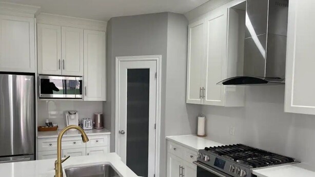 A modern kitchen with white cabinetry, a stainless steel refrigerator, a built-in microwave, a gas stove, and a sink with a gold faucet.