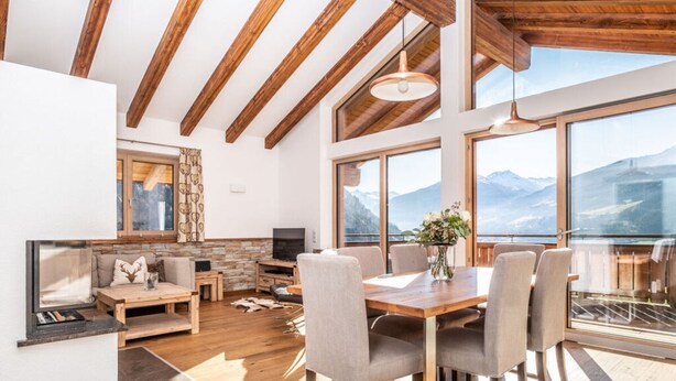 Amplia sala de estar con techo de madera, chimenea, revoco de piedra alrededor de la chimenea, televisor y mesa de comedor con sillas.