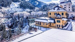 Un pueblo cubierto de nieve con un edificio amarillo destacado, rodeado de montañas y otros edificios.