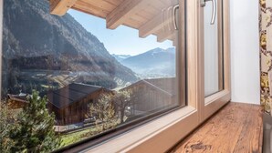 Ventana de madera con vistas a un paisaje montañoso, que incluye casas y cielo despejado.