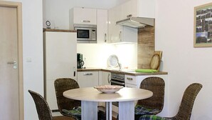 Ett kompakt kök med vita skåp, en mikrovågsugn och en spis. Där finns ett matbord med flätade stolar och kuddar med rutmönster.