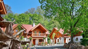 A row of wooden cabins with red roofs, surrounded by greenery and rocks. - Castle Chalet No. 19 (Ilsenburg)