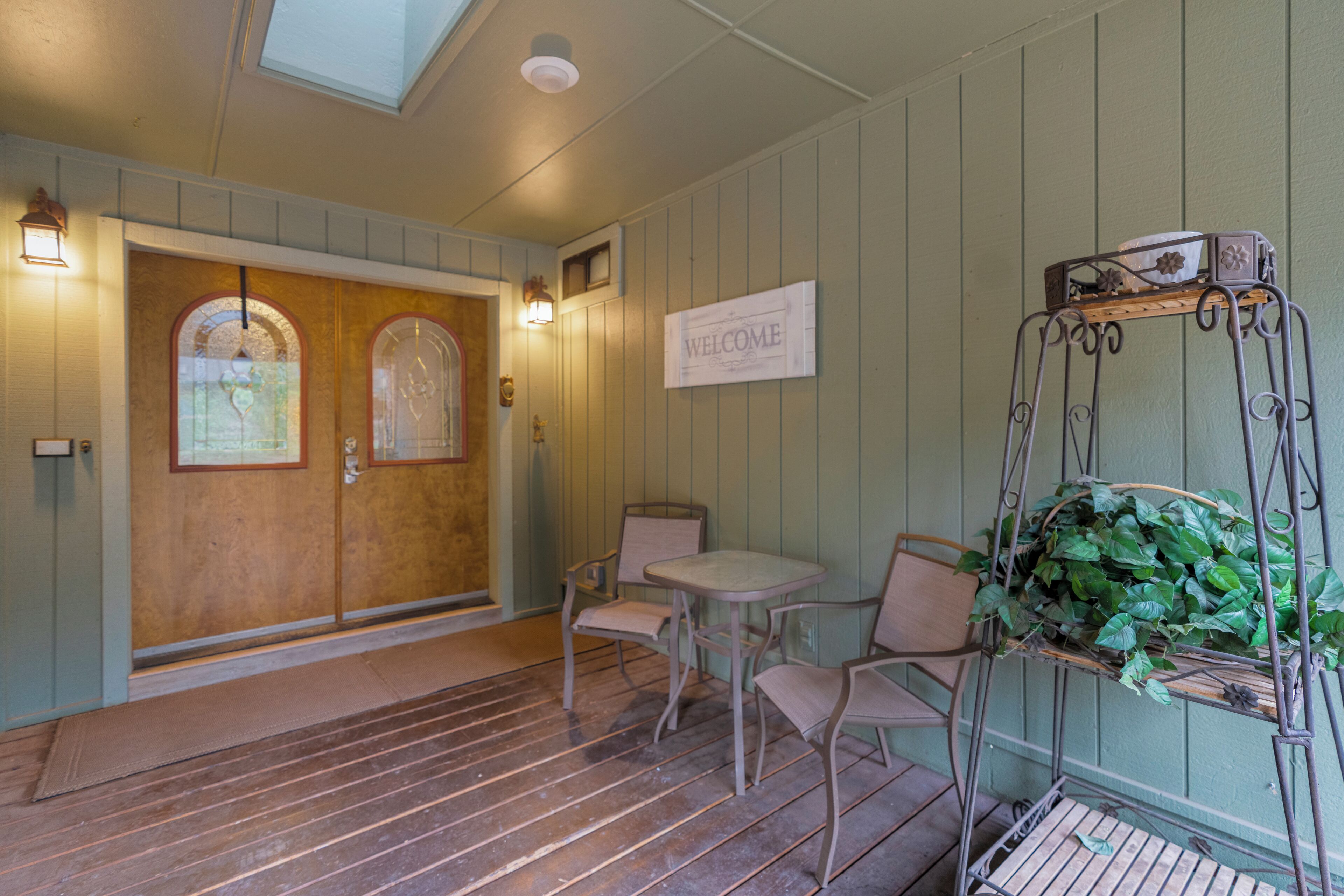 A wooden door with a window, a welcome sign, and a metal plant stand with a basket.