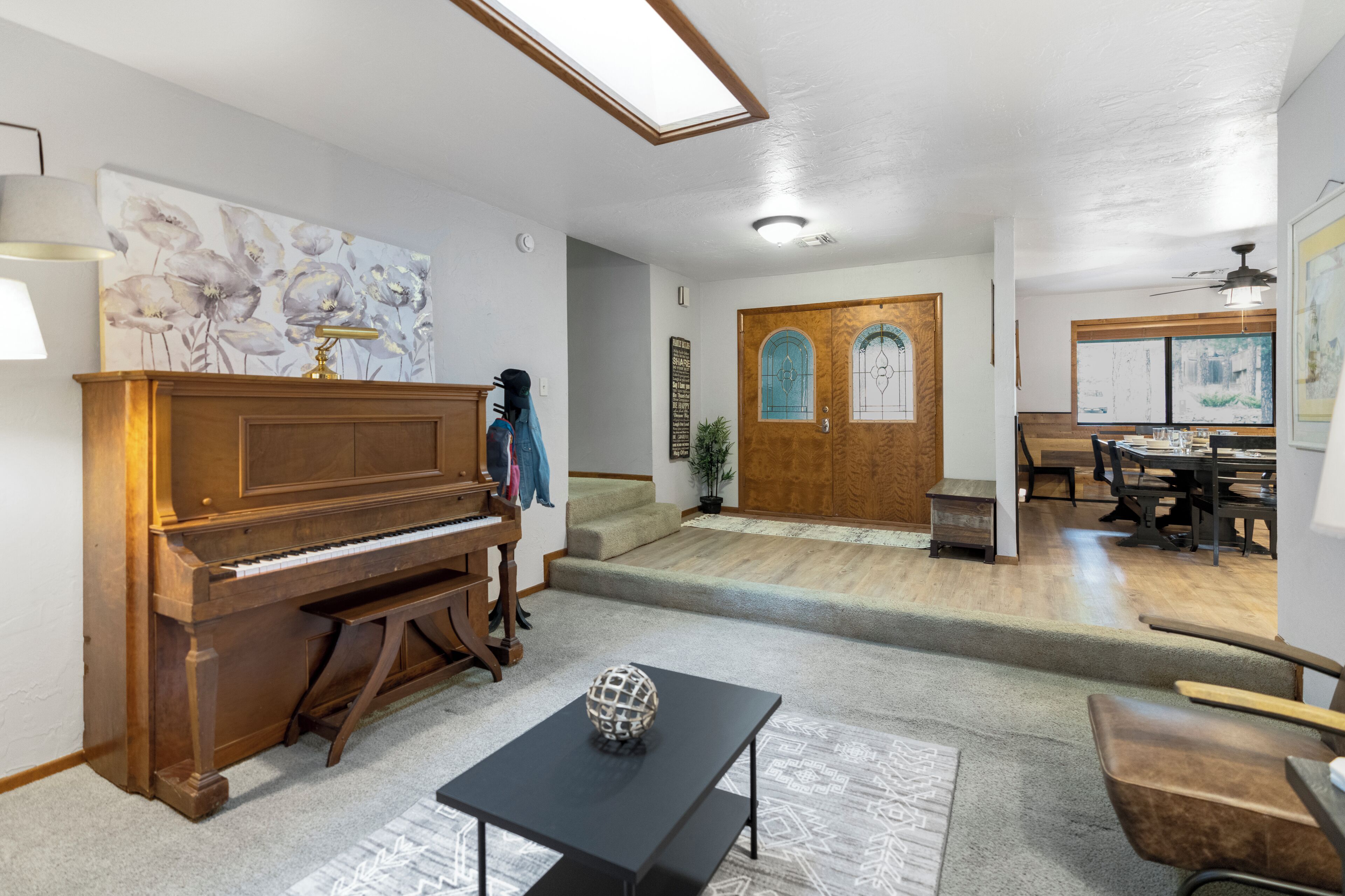 A spacious room with a grand piano, a dining area, and a staircase leading to a second floor.