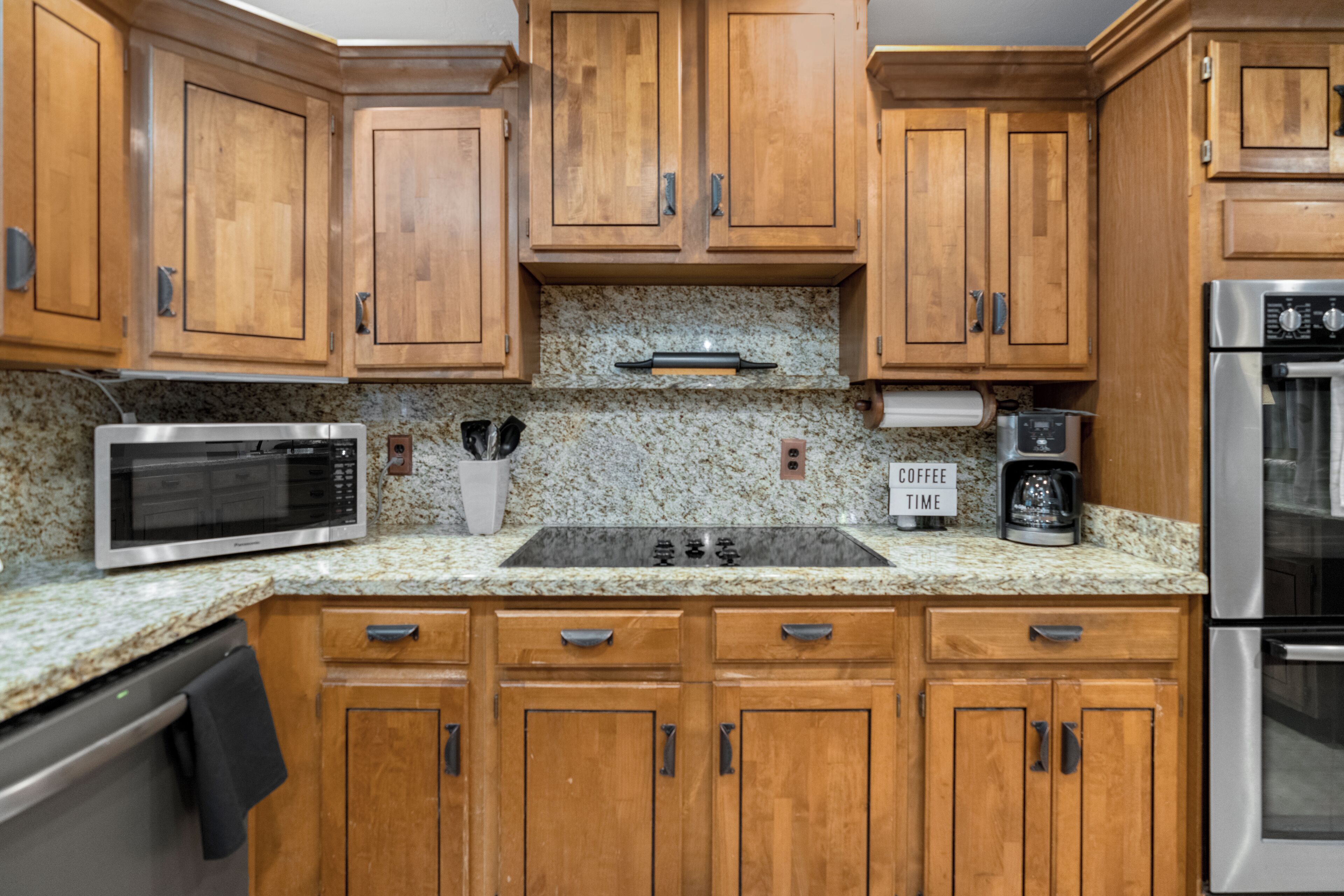 A kitchen with wooden cabinets, a granite countertop, a microwave, a coffee maker, and a stainless steel oven.