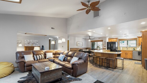 A spacious living room with a leather sofa, wooden coffee table, and a large ceiling fan.