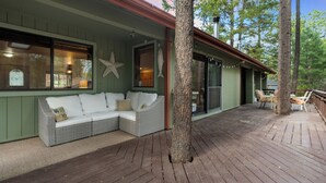 A covered outdoor seating area with a wicker sofa and chairs, a wooden deck, and a large tree trunk in the center.