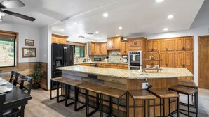 A modern kitchen with wooden cabinets, a large island with bar stools, stainless steel appliances, and a dining area with a table and chairs.