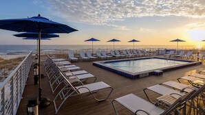 Uma área à beira da piscina com espreguiçadeiras e guarda-sóis, com vista para o oceano.