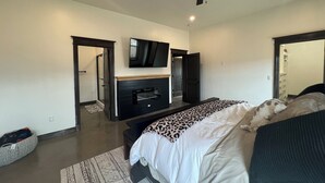 A modern bedroom with a bed, a TV mounted above a fireplace, a ceiling fan, and a walk-in closet. - Cozy retreat located in the perfect location for views of the mountains and lake (Eagle Nest)