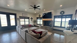 A spacious living room with a large sectional sofa, a fireplace, and a flat-screen TV mounted above it. - Cozy retreat located in the perfect location for views of the mountains and lake (Eagle Nest)