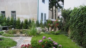 A garden with a stone pathway leading to a building with a white facade and green shutters. - Cosy Apartment in Eibenstock (Eibenstock)