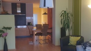 A modern living room with a dining area, a black leather sofa, a large potted plant, and a kitchen in the background. - Cosy Apartment in Eibenstock (Eibenstock)