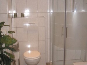 A bathroom with a toilet, a shower enclosure, and a potted plant.