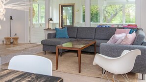 A modern living room with a grey sofa, a wooden coffee table, and a white chair. There is a bookshelf with books and a lamp. - 8 Person Holiday Home in Nordborg (Nordborg)