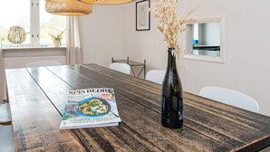 A wooden dining table with a magazine, a black vase with dried plants, and wicker pendant lights. - 8 Person Holiday Home in Nordborg (Nordborg)