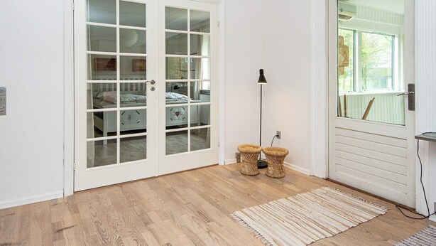 A room with a wooden floor, a white door with glass panels, a standing lamp, and a woven floor mat. - 8 Person Holiday Home in Nordborg (Nordborg)