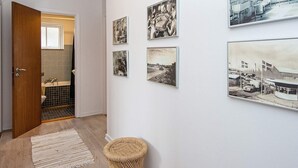 A hallway with a wooden door leading to a bathroom, a woven basket, and a series of black and white photographs on the wall. - 8 Person Holiday Home in Nordborg (Nordborg)