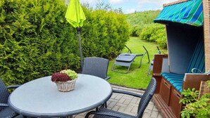 A patio with a round table, chairs, a wicker bench, and a bright green umbrella. - Tini - Haus Deichperle (Dornum)