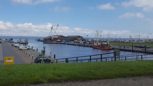 A marina with boats docked, a building with a crane, and a clear sky. - Tini - Haus Deichperle (Dornum)