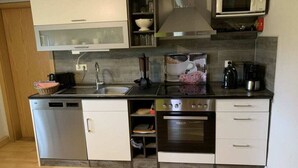 A compact kitchen with a dishwasher, stove, oven, microwave, and a sink. - Tini - Haus Deichperle (Dornum)