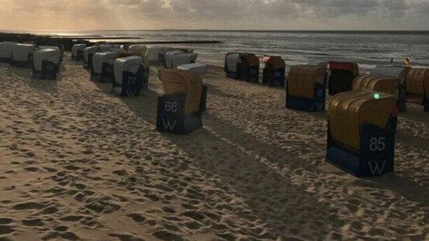 A beach with rows of tents labeled with numbers, a sandy beach, and the ocean in the background. - Tini - Haus Deichperle (Dornum)