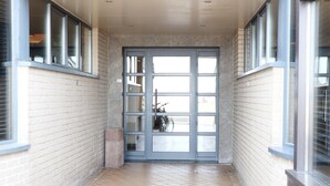 Un couloir avec un sol carrelé, une porte en verre à plusieurs panneaux et un vélo garé à l’extérieur.