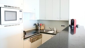 Une cuisine moderne avec des meubles blancs, un plan de travail noir, un four à micro-ondes, un évier et un appareil électroménager rouge.