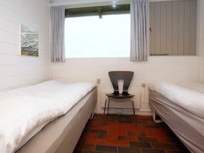 Een kleine, schone kamer met twee enkele bedden, een stoel en een raam met gordijnen.