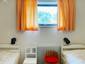 A room with two beds, a small table, a chair with a red cushion, and a window with curtains. - 6 Person Holiday Home in Uddevalla-by Traum (Uddevalla)