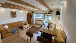 Amplia sala de estar con techo de madera, un sofá grande, una mesa de comedor y vistas al exterior.