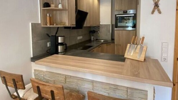 Una cocina moderna con armarios de madera, una isla central con taburetes altos y electrodomésticos integrados.