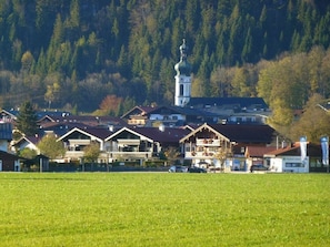 A rural village with traditional wooden houses, a church with a bell tower, and a large open field in the foreground. - Berggluck Comfortable Holiday Residence (Reit im Winkl)